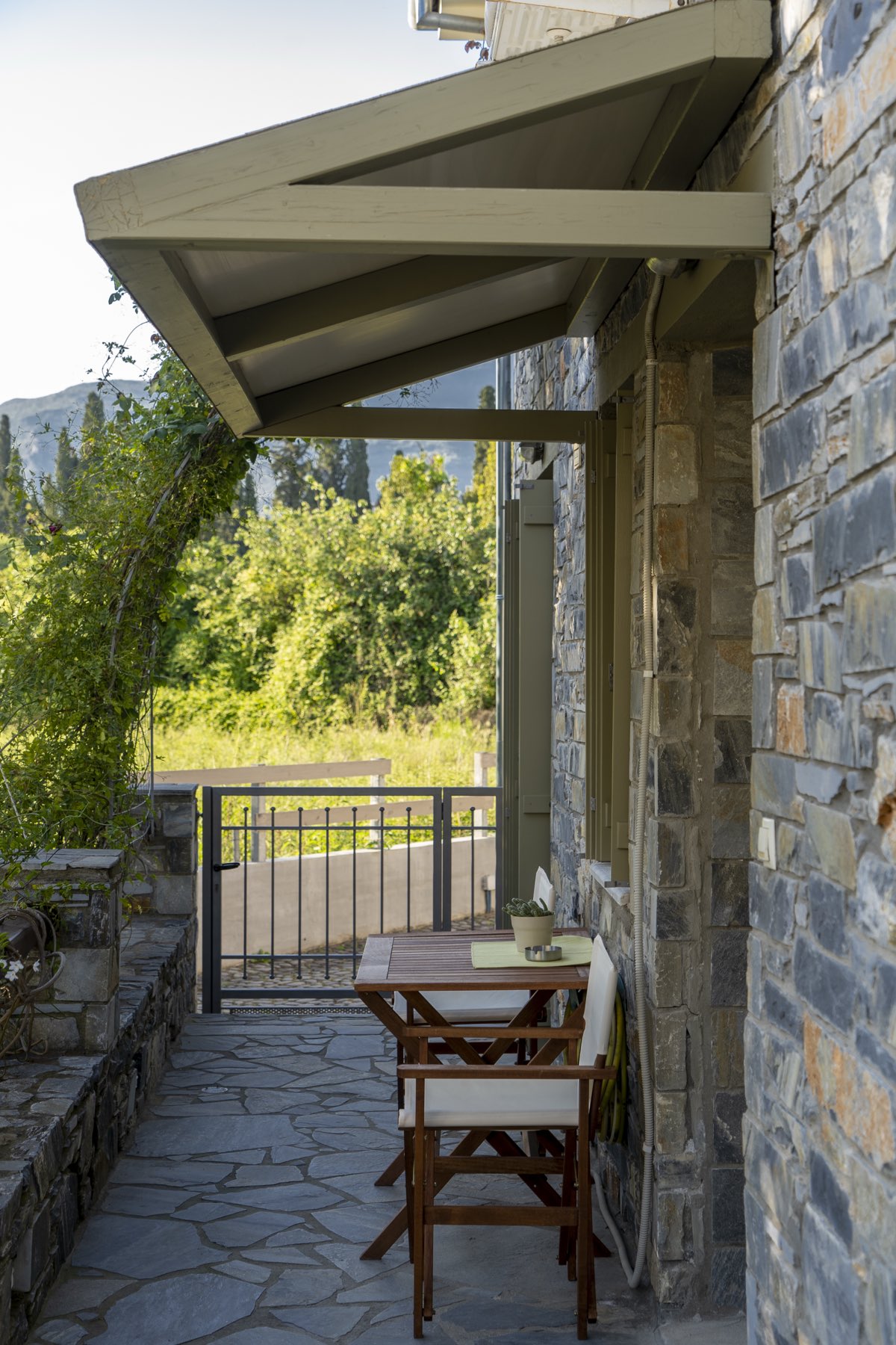 A covered stone porch with a small table, looking out over the garden to the mountain