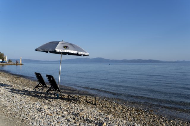 A parasol and two loungers on the pebble beach, the gulf beyond