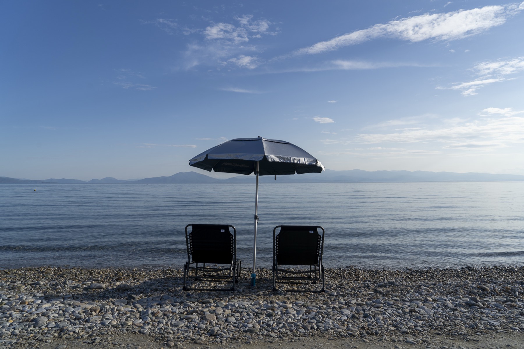 A parasol and two loungers on the pebble beach in front of the villa, early morning